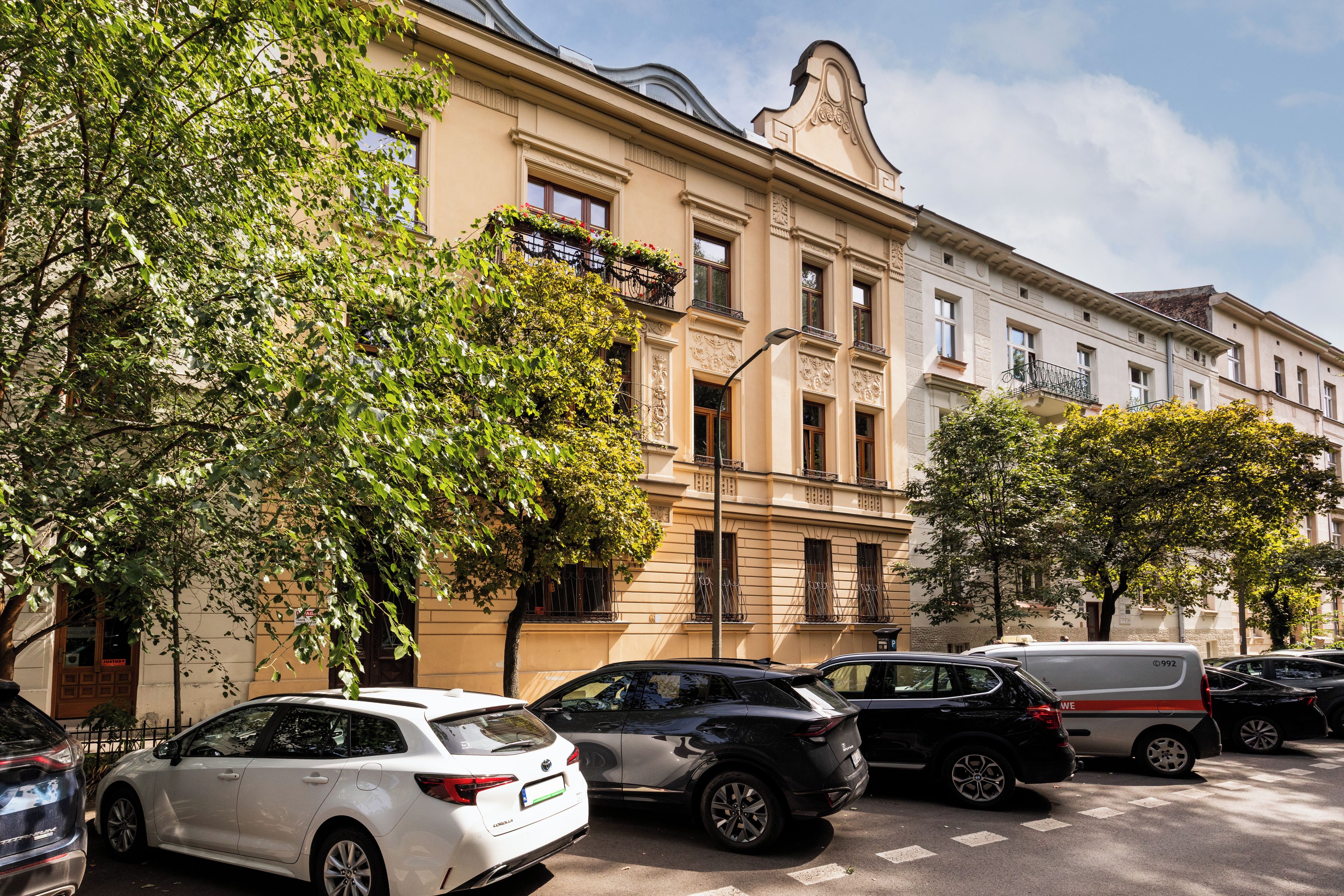 A street view with parked cars and a building with ornate architectural details.
