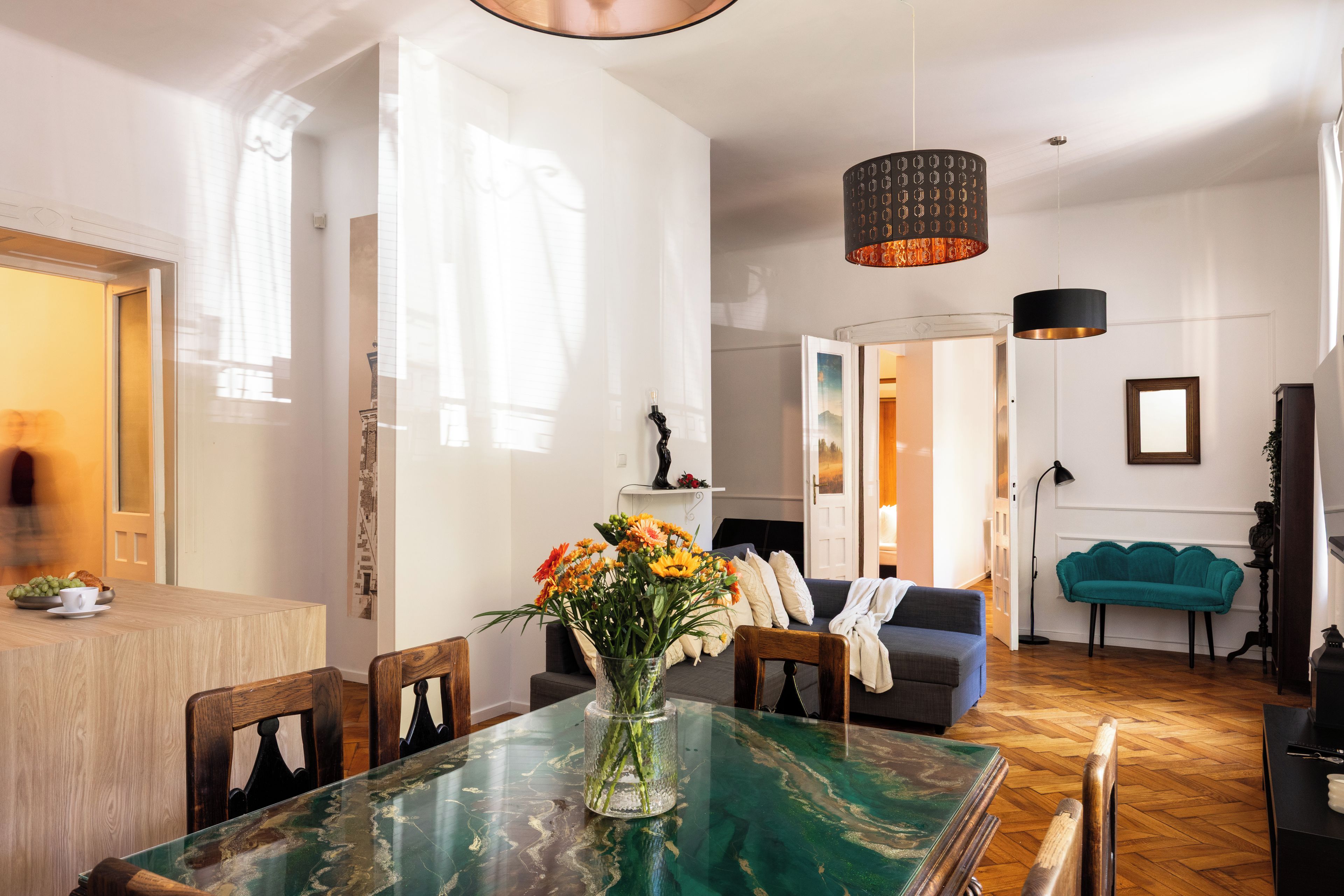 A modern living room with a glass-top dining table, a sofa, and a teal armchair.