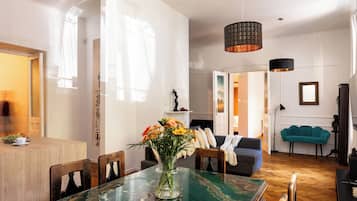 A modern living room with a glass-top dining table, a sofa, and a teal armchair.
