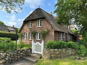 A traditional brick house with a thatched roof, a stone wall, and a white gate. - Westerhus Nieblum (Nieblum)