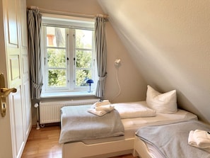 A bedroom with two beds, a window with curtains, a radiator, and a wall socket. - Westerhus Nieblum (Nieblum)