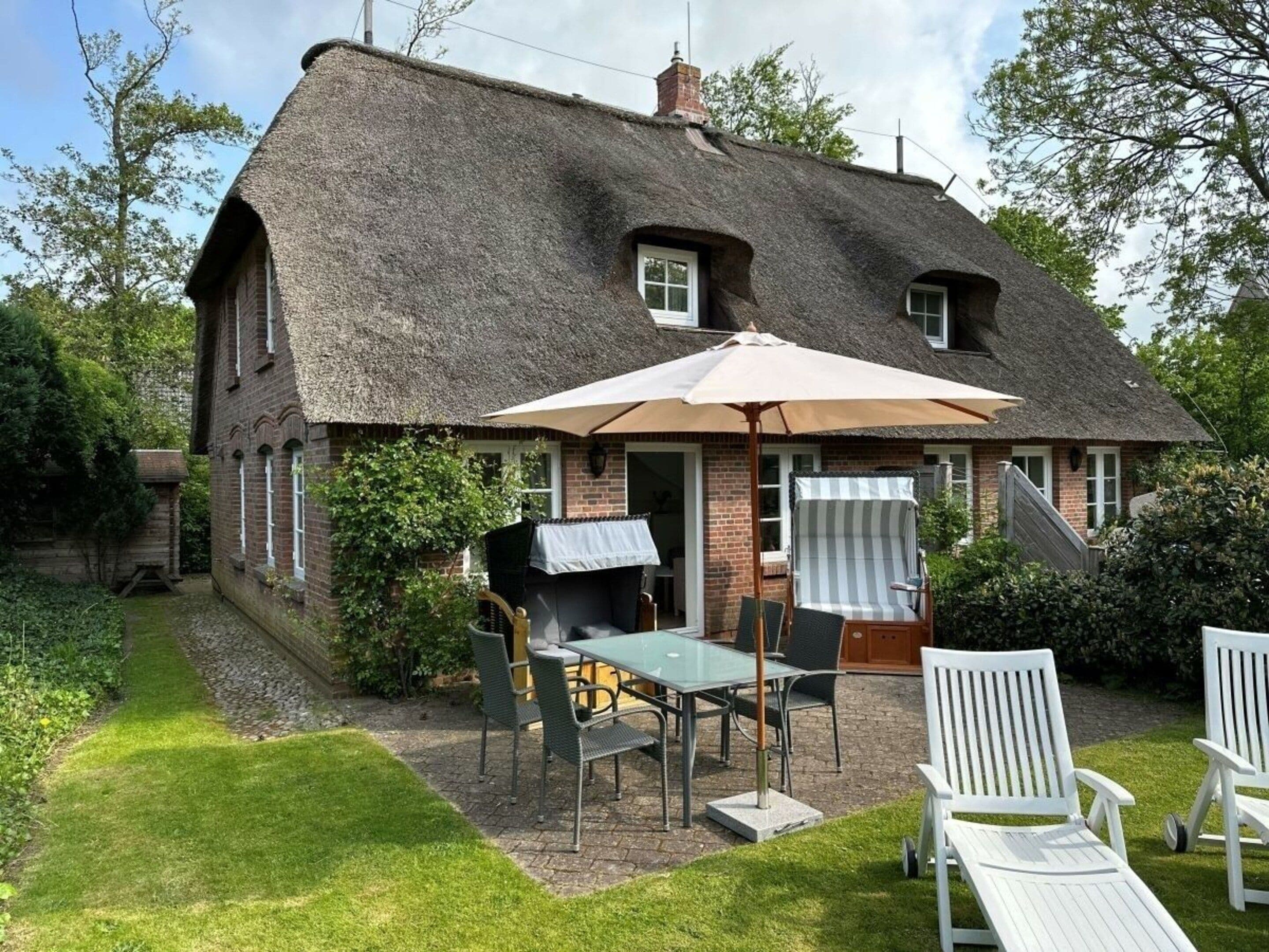 A thatched-roof house with a patio area, a table, chairs, and a striped umbrella.