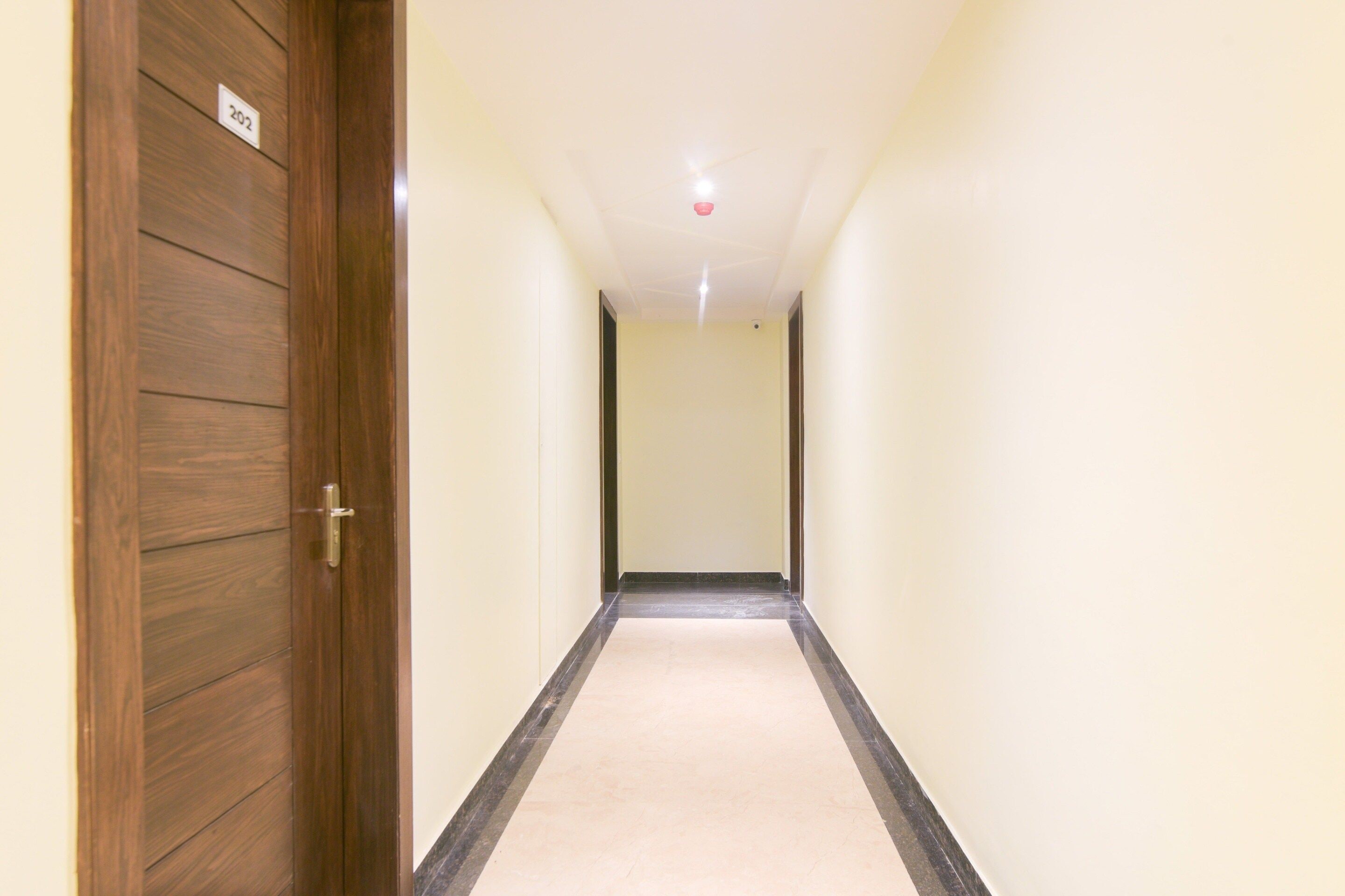 A hallway with a wooden door on the left, a white wall, and a light-colored carpet.
