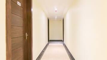 A hallway with a wooden door on the left, a white wall, and a light-colored carpet.