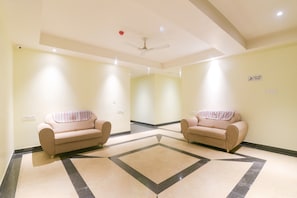 Un hall de hotel con dos sillones, una alfombra estampada y un ventilador de techo.