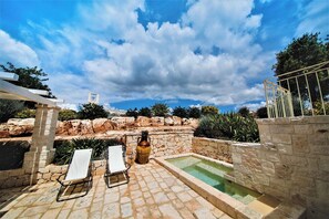 Un espace piscine extérieur agrémenté de murs en pierre, d’une pergola et de chaises longues.