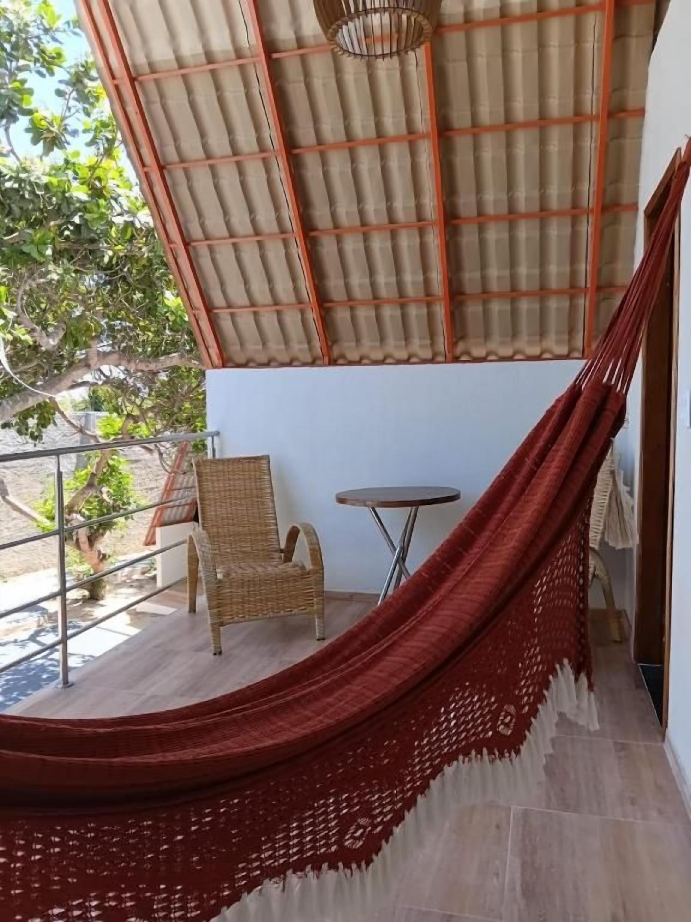 A hammock, a wicker chair, and a small round table on a balcony with a metal railing.