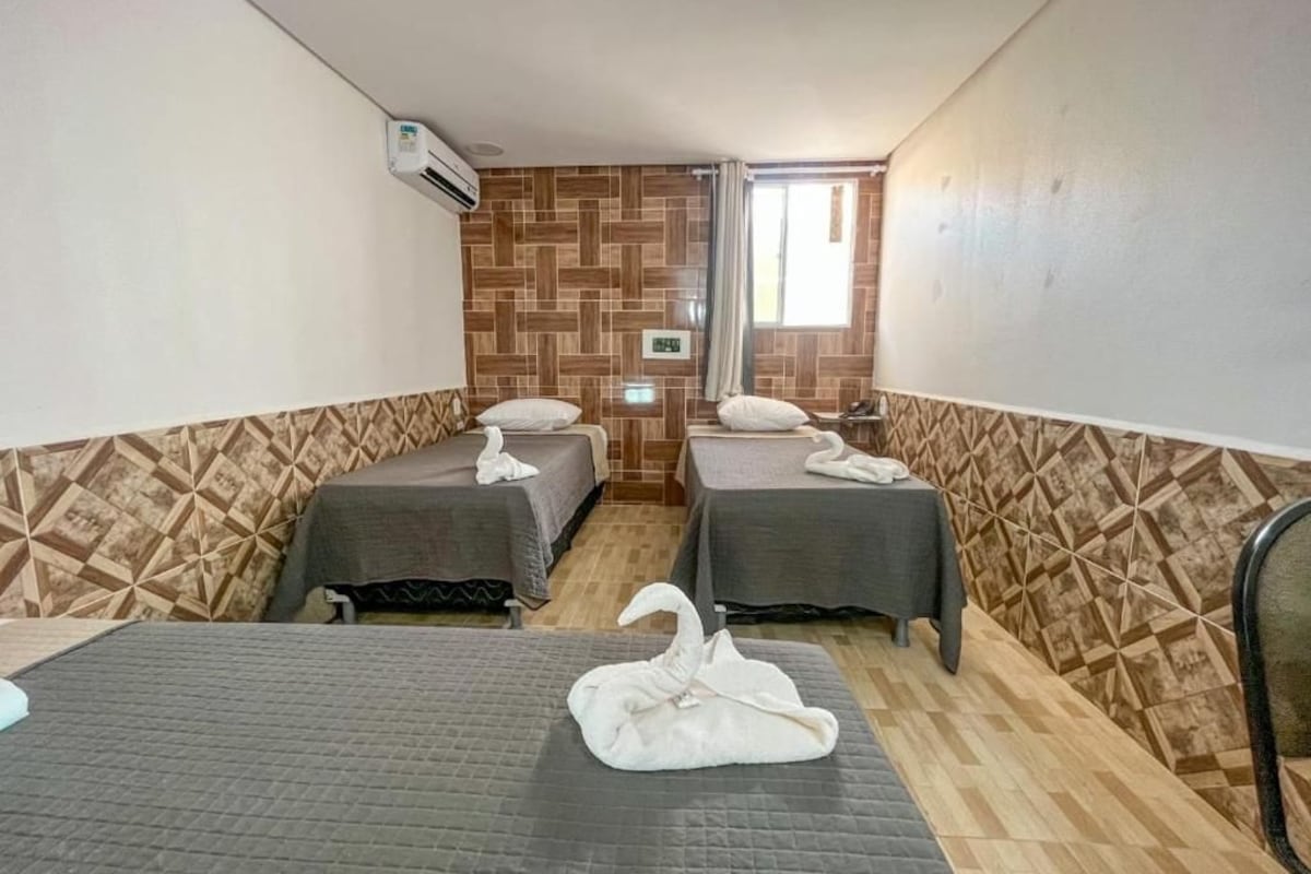 Habitación de hotel con dos camas, aire acondicionado de pared y ventana con cortinas.