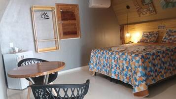 Un dormitorio con una cama, cabecera de madera, una mesa con sillas y un aire acondicionado instalado en la pared.