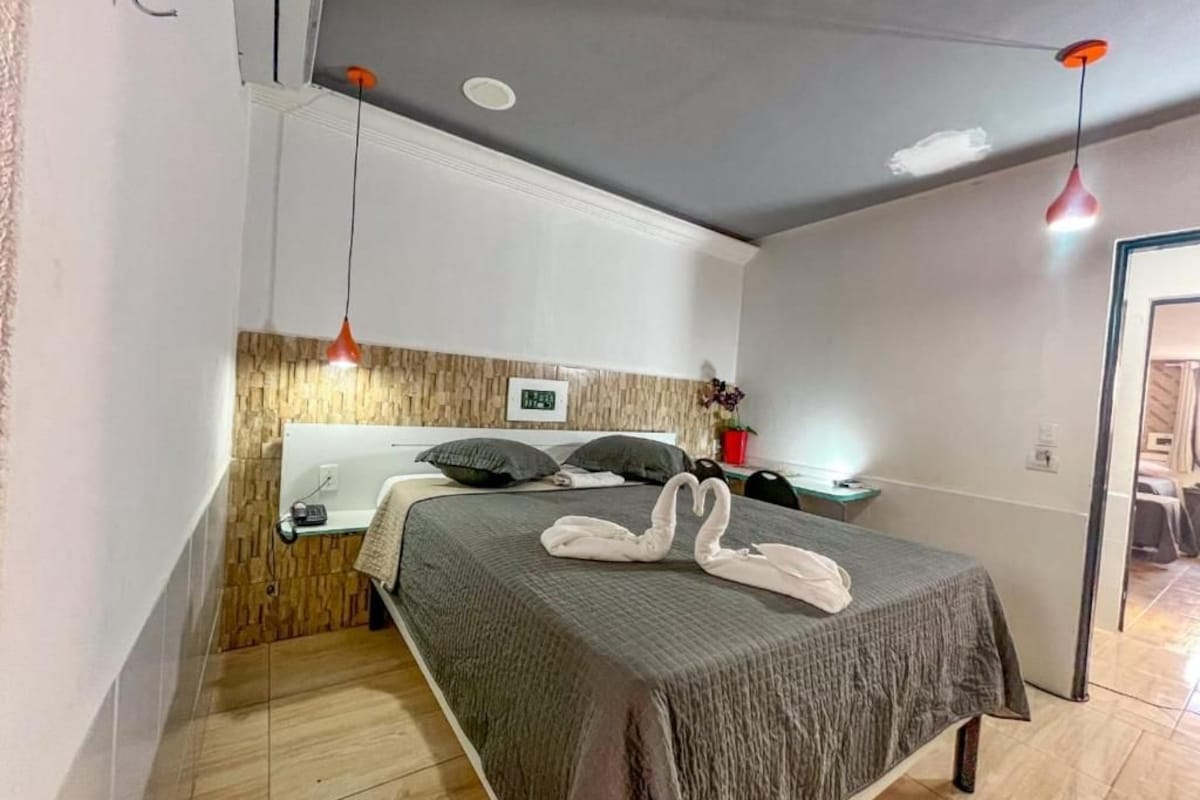 Una habitación de hotel con una cama, una mesita de noche, una lámpara y un reloj de pared.