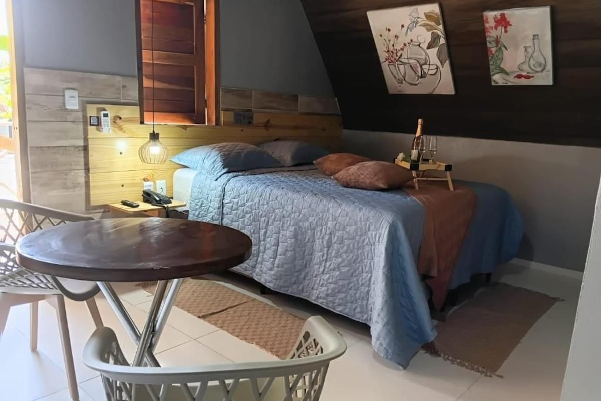 Un dormitorio con cama, mesita de noche, lámpara y una obra de arte en la pared.