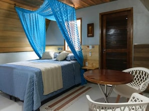 Un dormitorio con cama, mesita de noche, silla y ventana con cortinas.