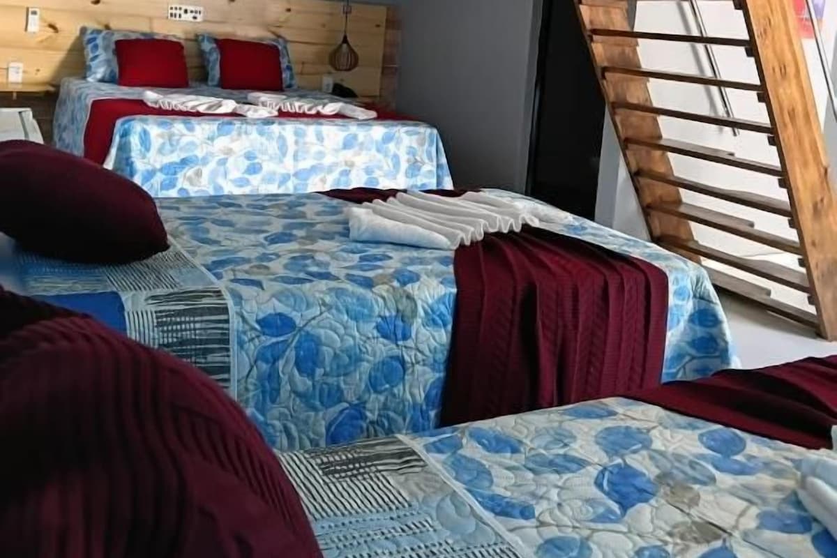 Habitación con dos camas, cabecera de madera, ventilador de techo y techo inclinado.