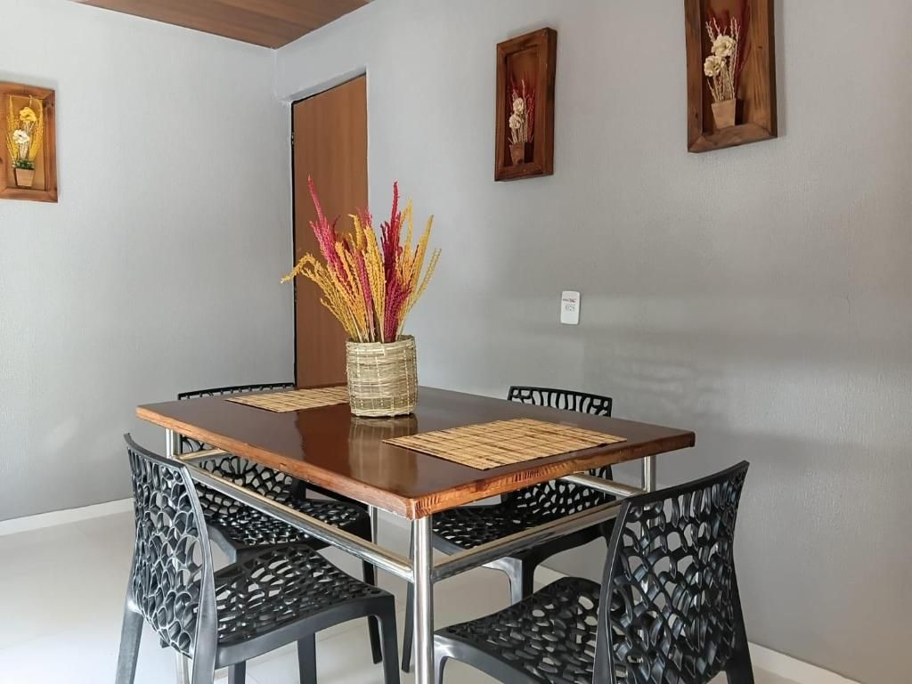 Un comedor con una mesa de madera, sillas negras y un florero con flores secas.