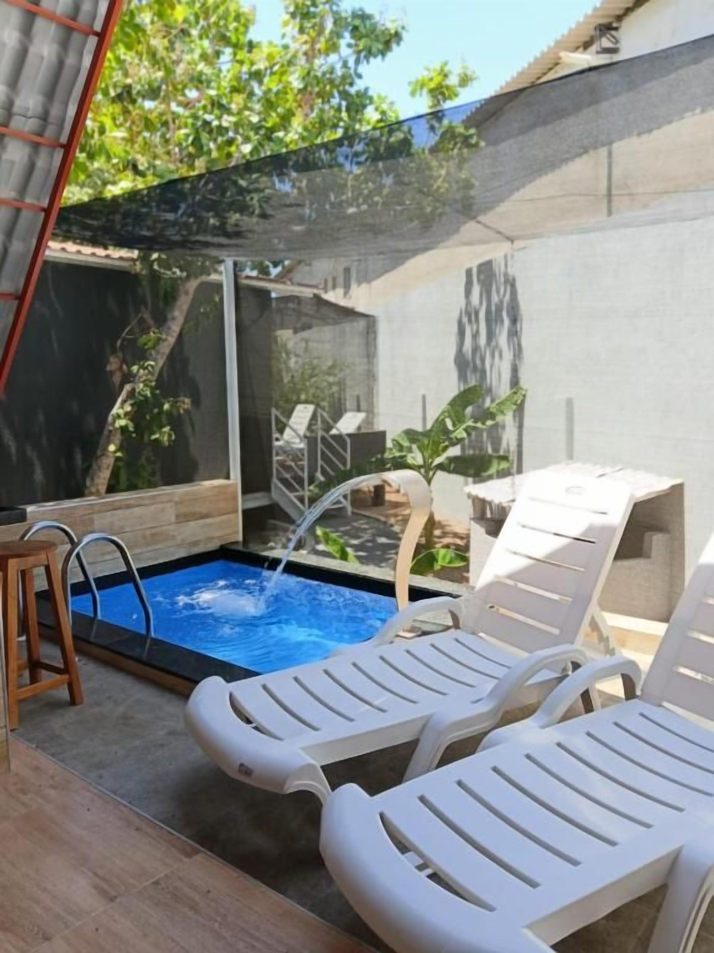Piscina com um elemento aquático, rodeada por cadeiras de descanso brancas e uma pequena mesa.