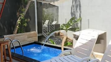 Piscina com um elemento aquático, rodeada por cadeiras de descanso brancas e uma pequena mesa.