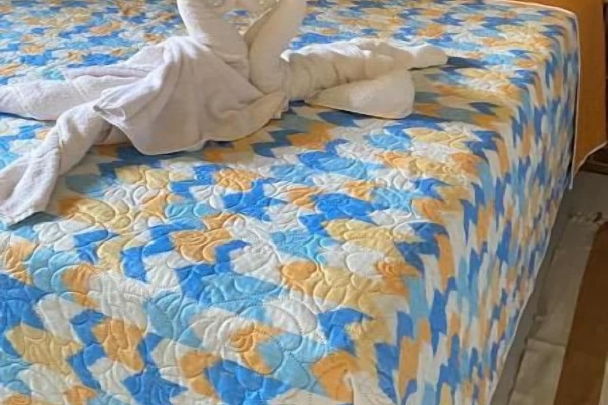 Una cama con una colcha azul y amarilla estampada, dos almohadas rojo oscuro y una toalla blanca doblada en forma de cisnes.