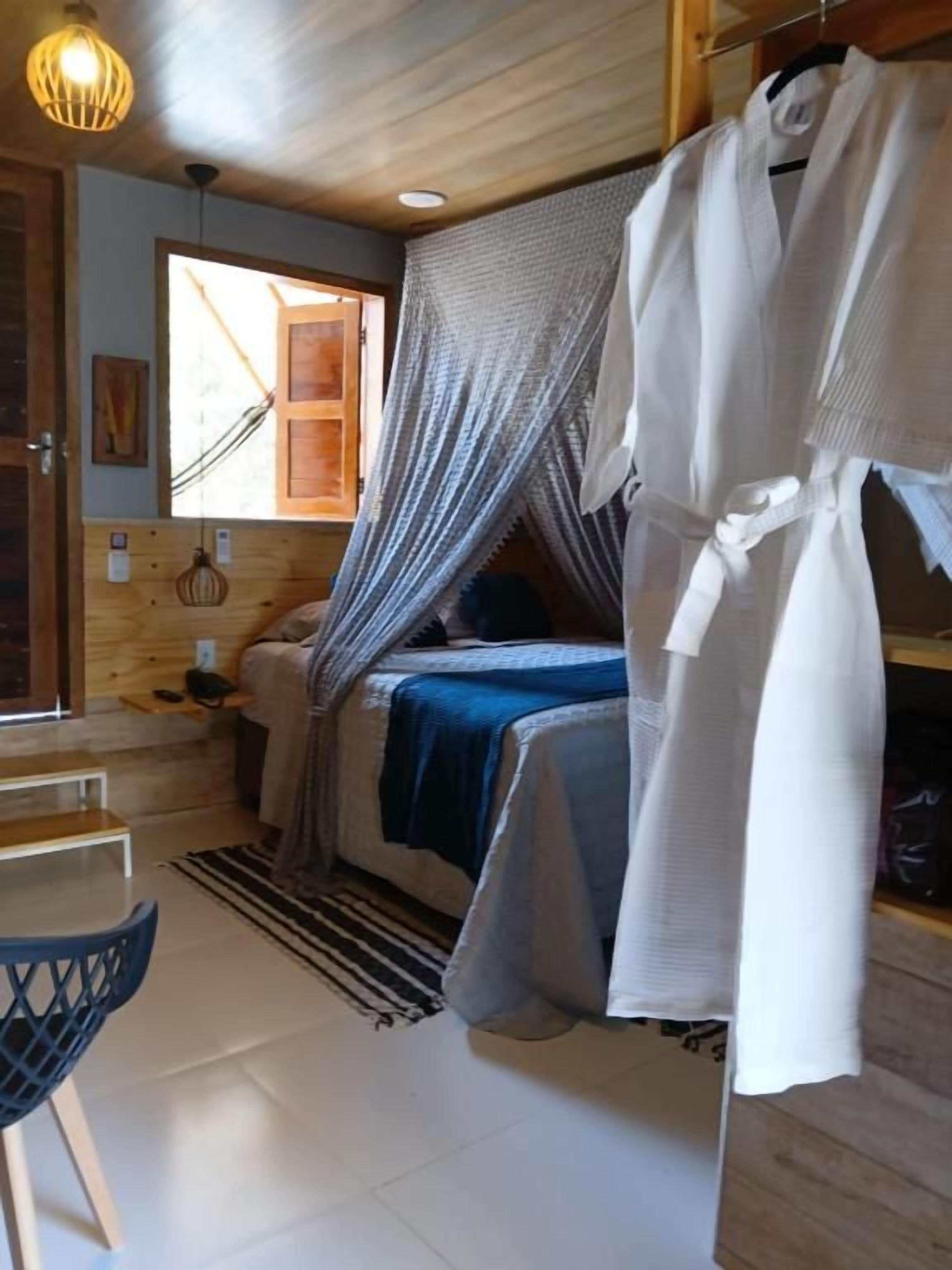 Quarto com cama, roupão pendurado, cadeira e janela.