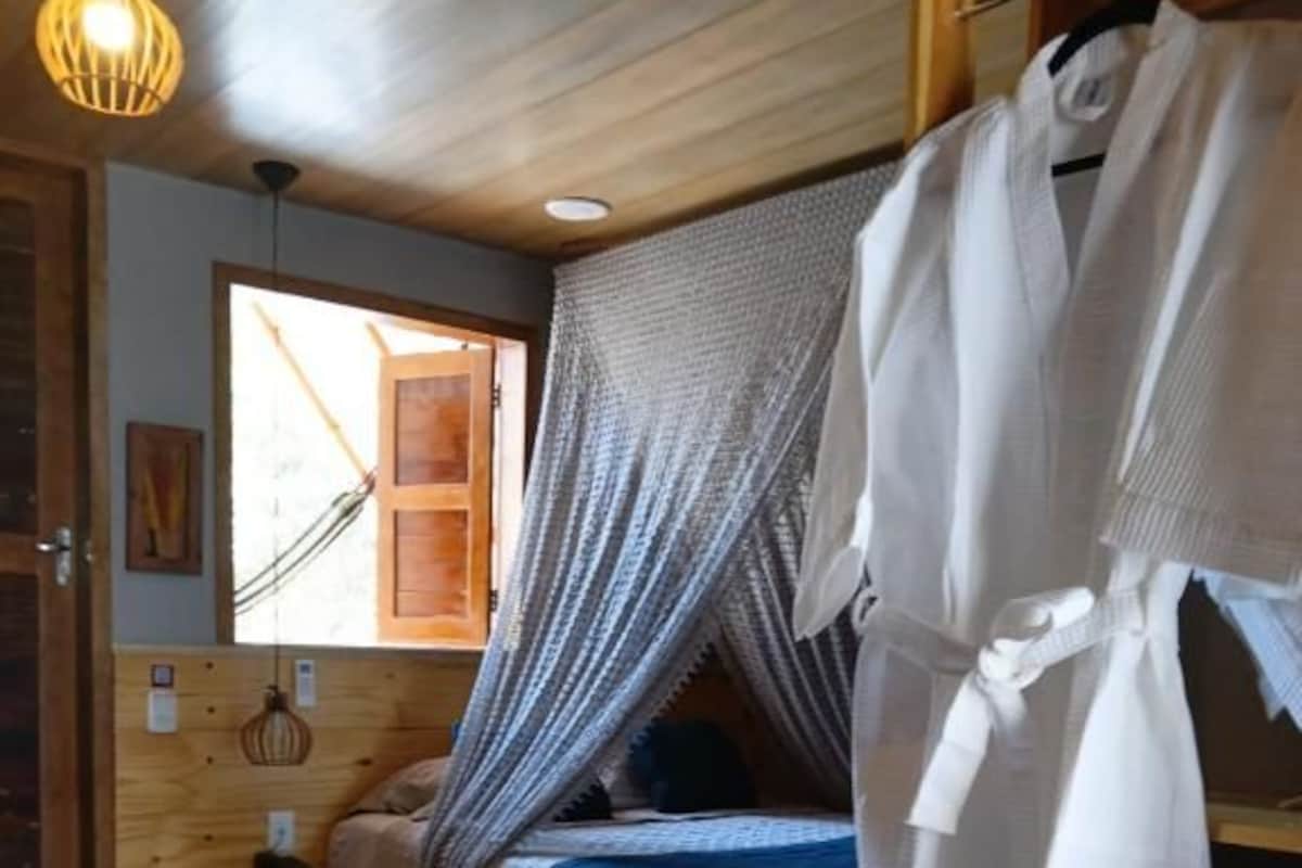 Un dormitorio con una cama, una percha, una silla y un ventanal.