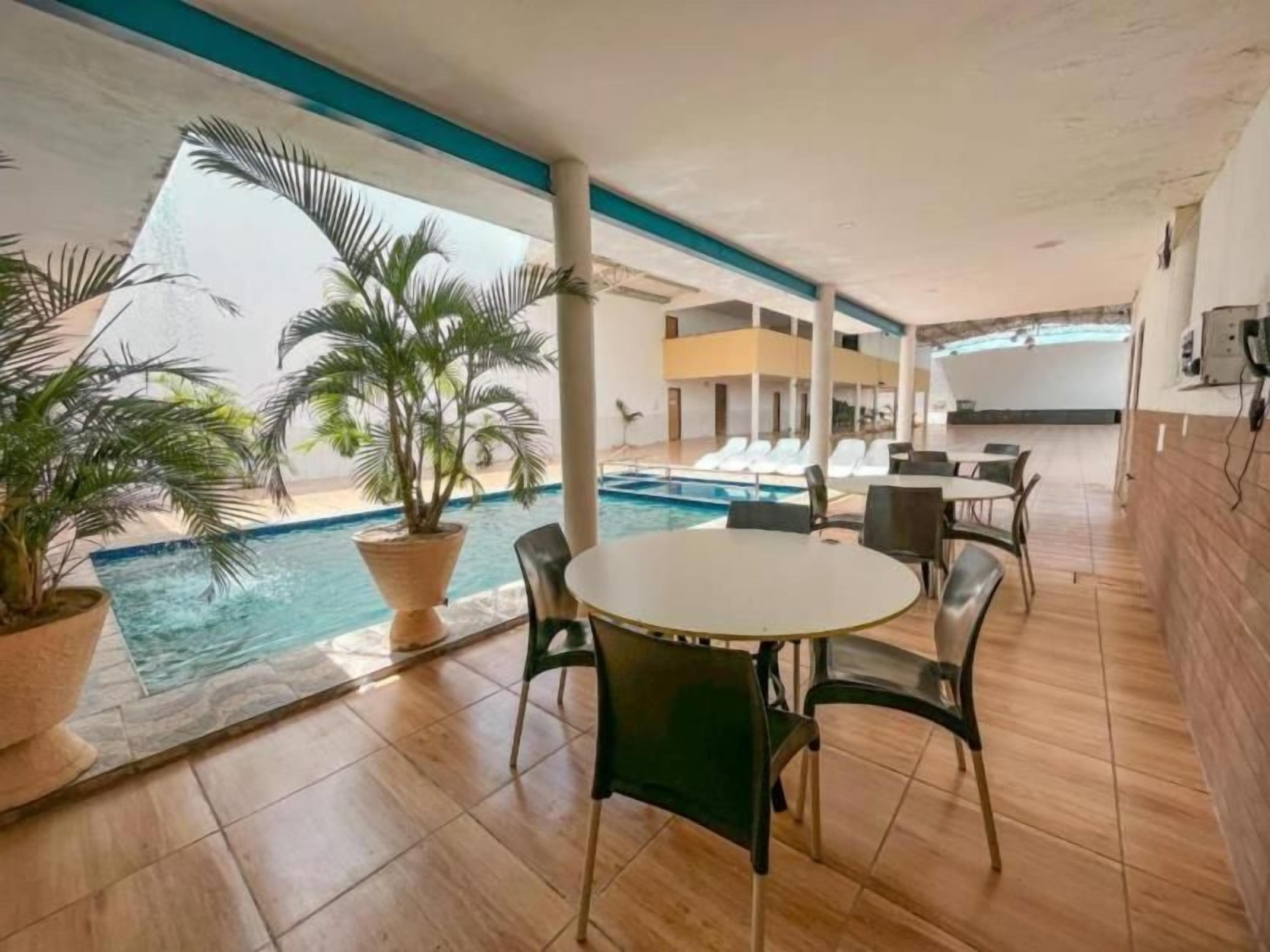 Zona junto a la piscina con una mesa redonda y sillas, plantas en macetas y vistas a la piscina.