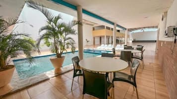 Zona junto a la piscina con una mesa redonda y sillas, plantas en macetas y vistas a la piscina.