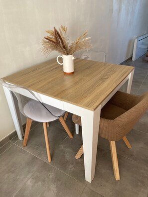 Een eettafel met een wit onderstel en een houten blad, met een stoel en een vaas met gedroogde planten.