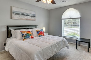 A bedroom with a bed, a ceiling fan, a window with blinds, and a painting on the wall. - Modern Galveston Retreat Near Beach, Strand & Pier (Galveston)