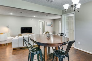 A modern dining area with a round table, black chairs, a flat-screen TV, and a ceiling light fixture. - Modern Galveston Retreat Near Beach, Strand & Pier (Galveston)