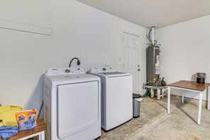 Ein Waschraum mit zwei Waschmaschinen mit Frontlader, einem Warmwasserbereiter und einem kleinen Tisch mit einem Mülleimer.