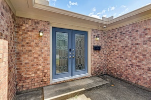 A two-door entrance with a brick wall, a small porch, and a security camera. - Modern Galveston Retreat Near Beach, Strand & Pier (Galveston)