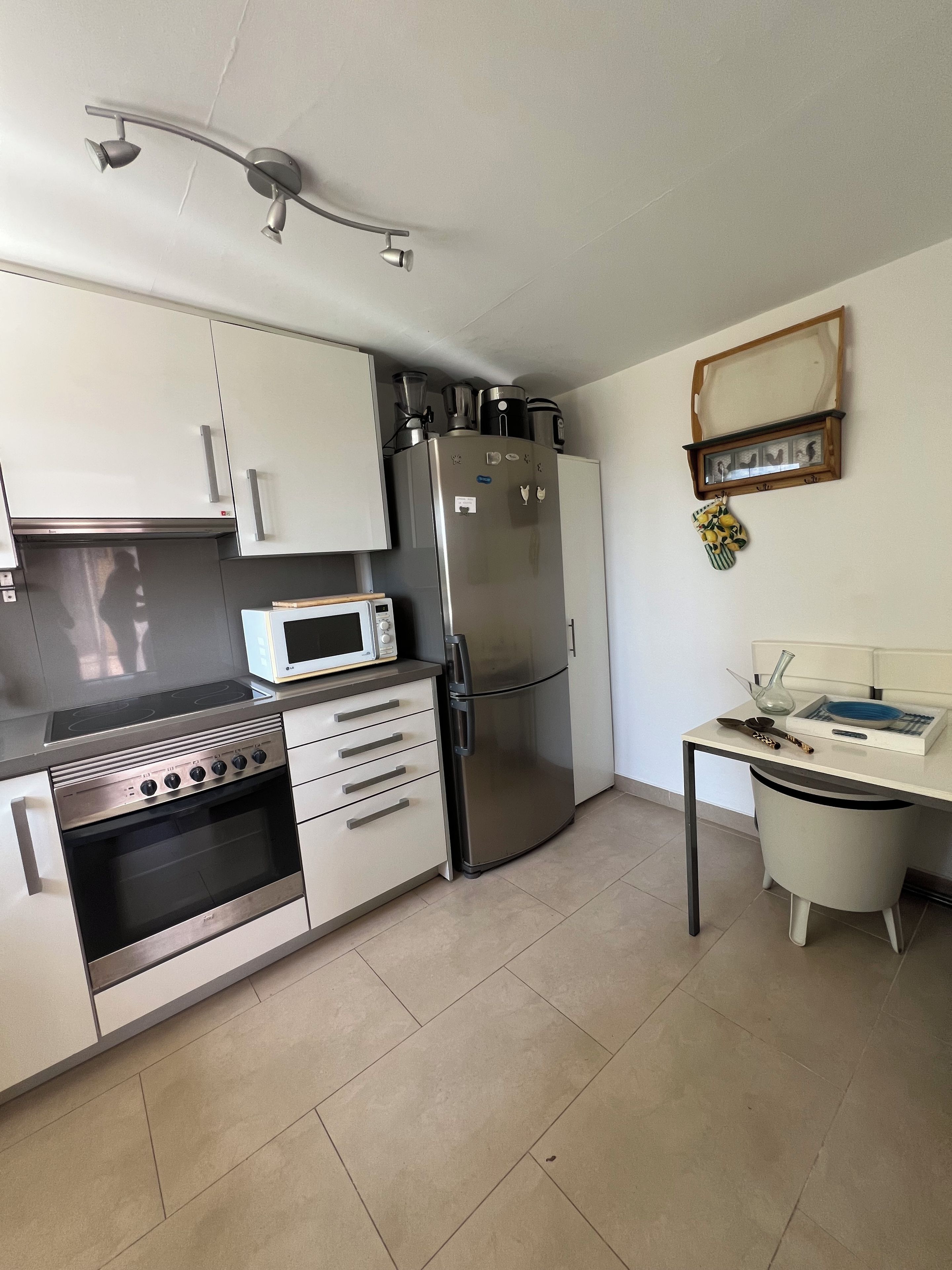 A compact kitchen with a built-in oven, microwave, refrigerator, and a small dining table with a chair.