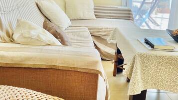 A room with a sofa set, a wicker chair, a small table with a book, and a round mirror on the wall.