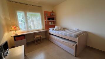 A bedroom with a bed, desk, chair, and a shelf with books.