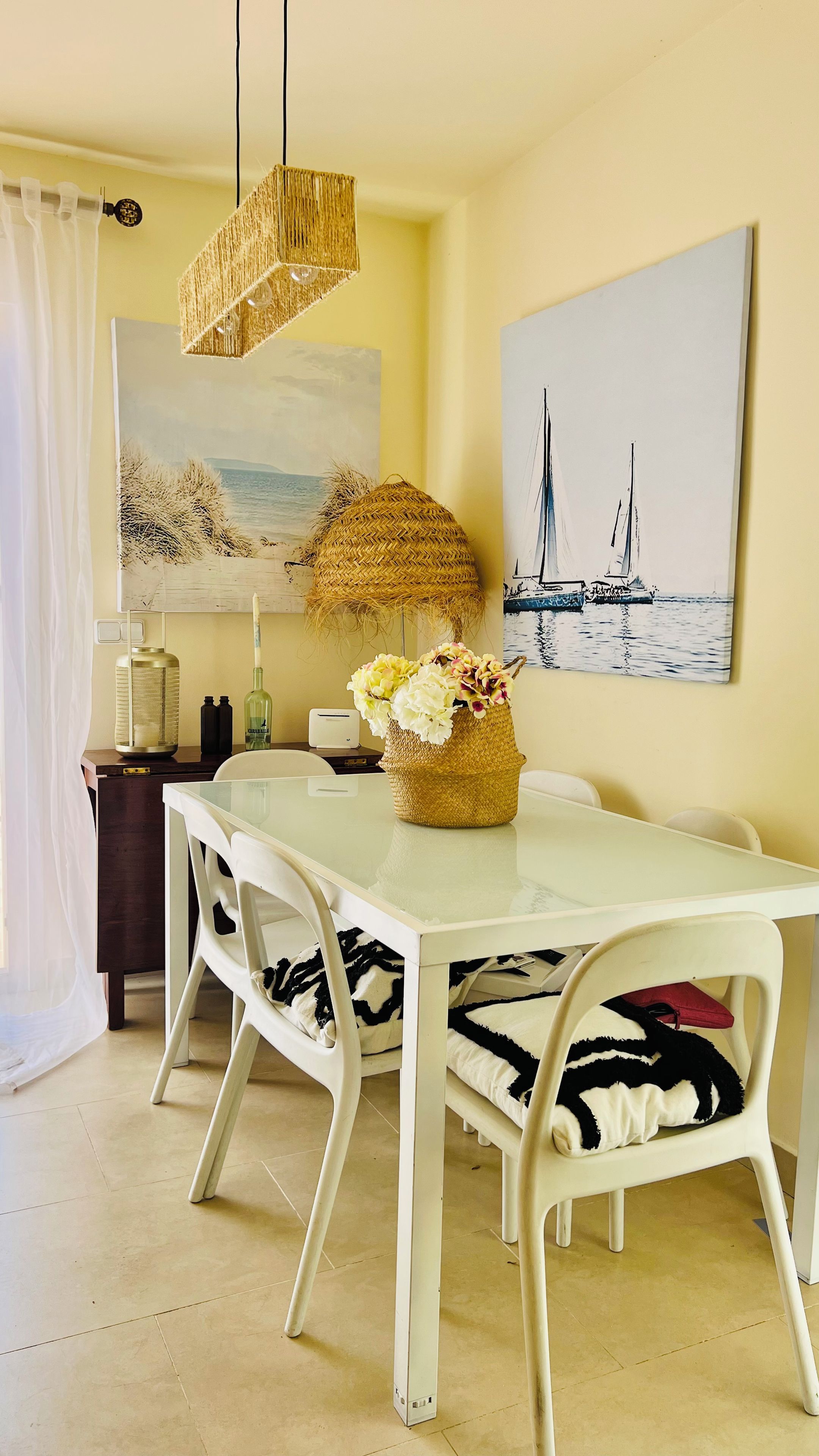 A dining area with a white table, wicker centerpiece, and nautical-themed artwork.