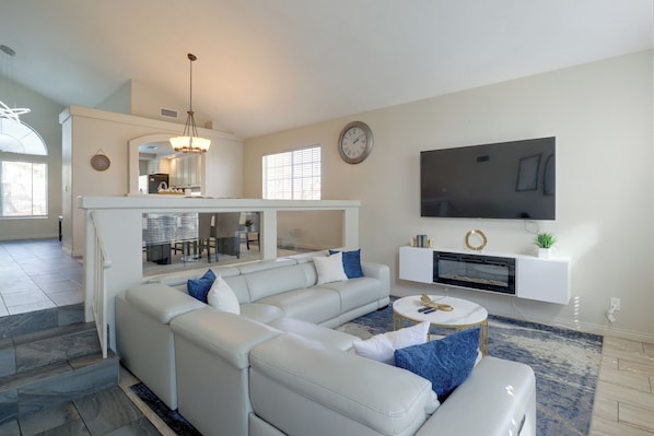 A modern living room with a sectional sofa, a flat-screen TV, a fireplace, and a dining area visible through a glass partition.