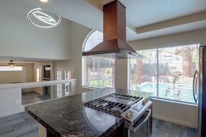 A kitchen with a central island, a stainless steel range, and a large window overlooking a backyard.