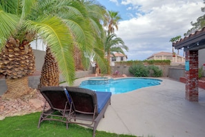 A backyard with a swimming pool, a palm tree, and a lounge chair.