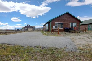 A rural property with a gravel driveway leading to a wooden house with a green roof, a fenced yard, and a clear sky. - Walkable Fairplay Home w/ Mtn Views! (Fairplay)