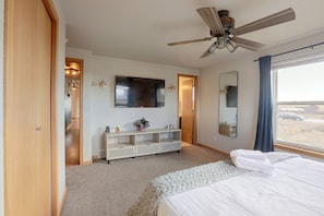 Quarto com cama, ventilador de teto, televisão, espelho e janela com cortinas.