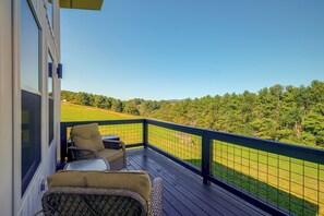 Ein Balkon mit Korbmöbeln, Blick auf eine grüne Landschaft und einen klaren Himmel.