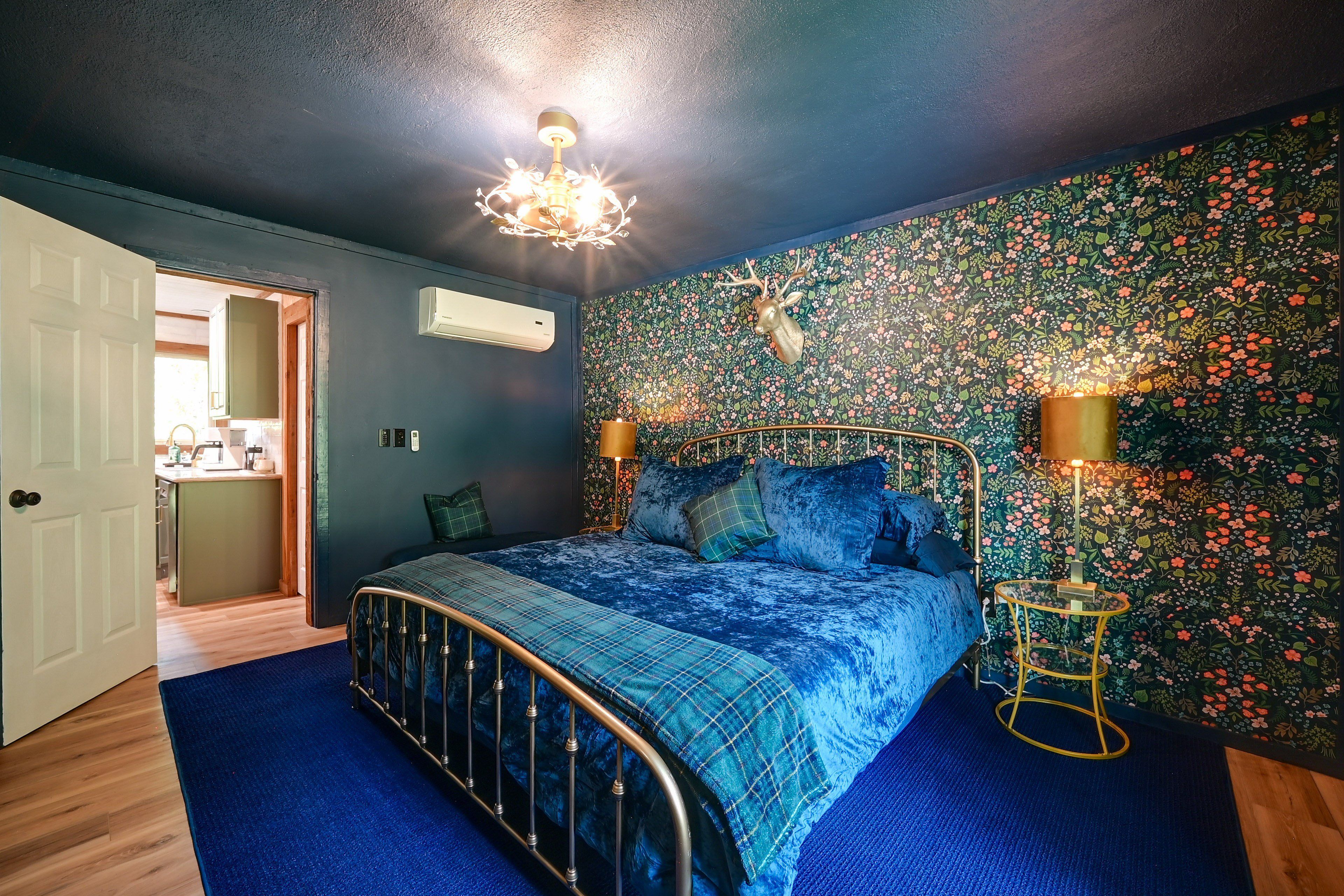 A bedroom with a bed, a chandelier, a wall-mounted air conditioner, and a floral wallpaper.