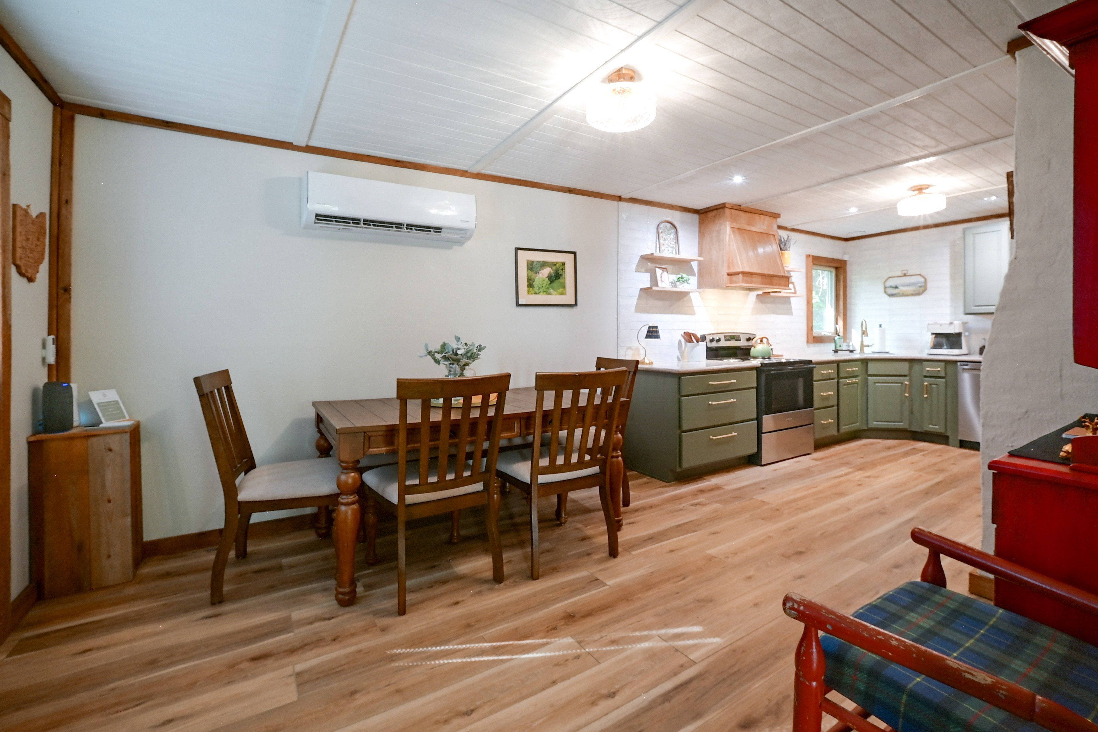 A dining area with wooden furniture, a kitchen with green cabinets, and an air conditioning unit on the wall.