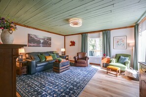 Una sala de estar con un tapete azul estampado, un sofá de cuero, un sillón de madera y un sillón verde.