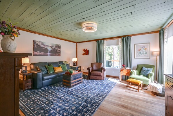 A living room with a blue patterned rug, a leather sofa, a wooden armchair, and a green armchair. - Hocking Hills Area Cabin Walk to National Forest (Nelsonville)