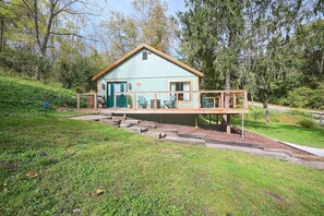 Eine kleine, hellblaue Holzhütte mit einer Holzterrasse und einer grünen Tür, umgeben von Bäumen und einer Rasenfläche.