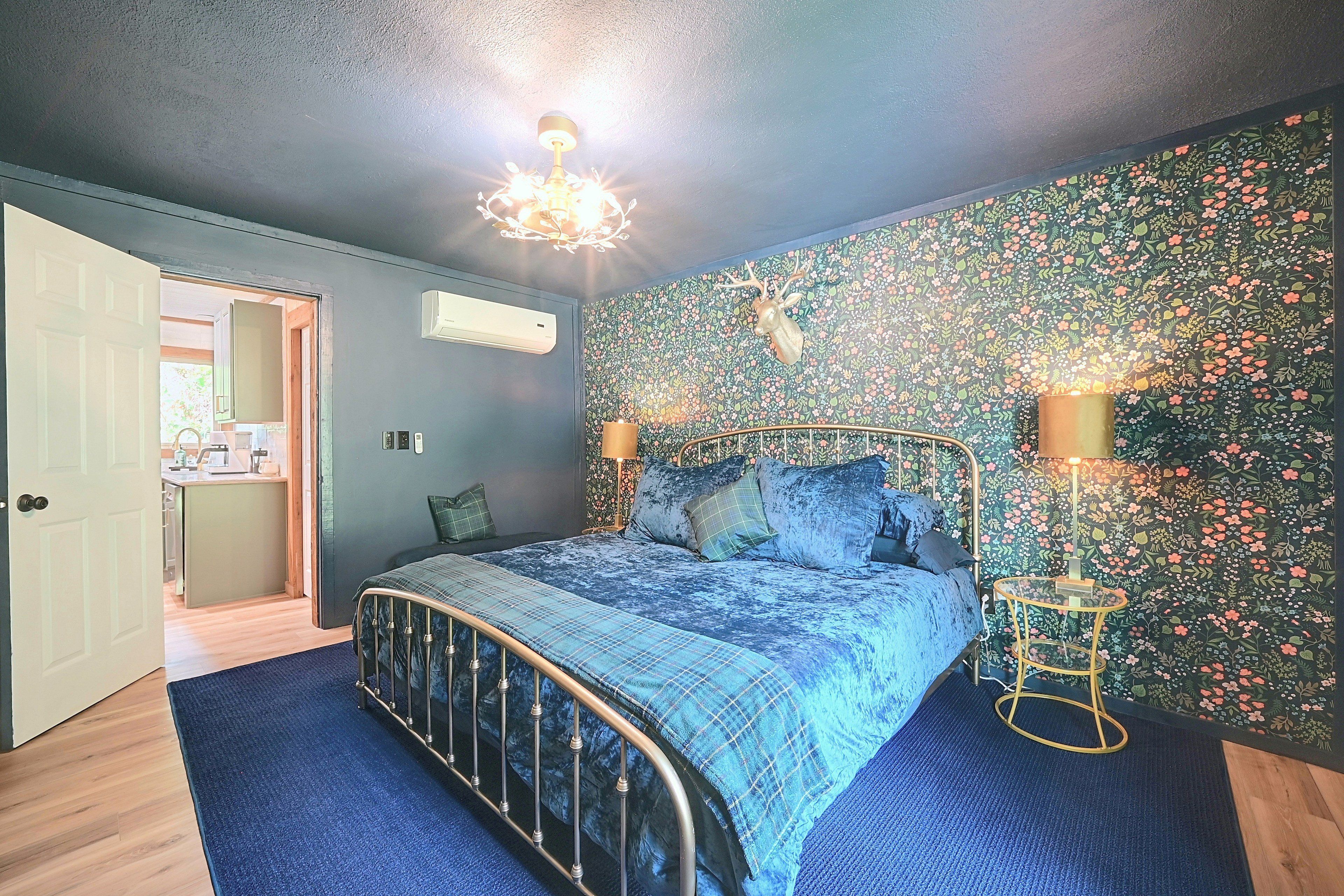 A bedroom with a bed, a wall-mounted air conditioner, a ceiling light fixture, and a floral-patterned wall.