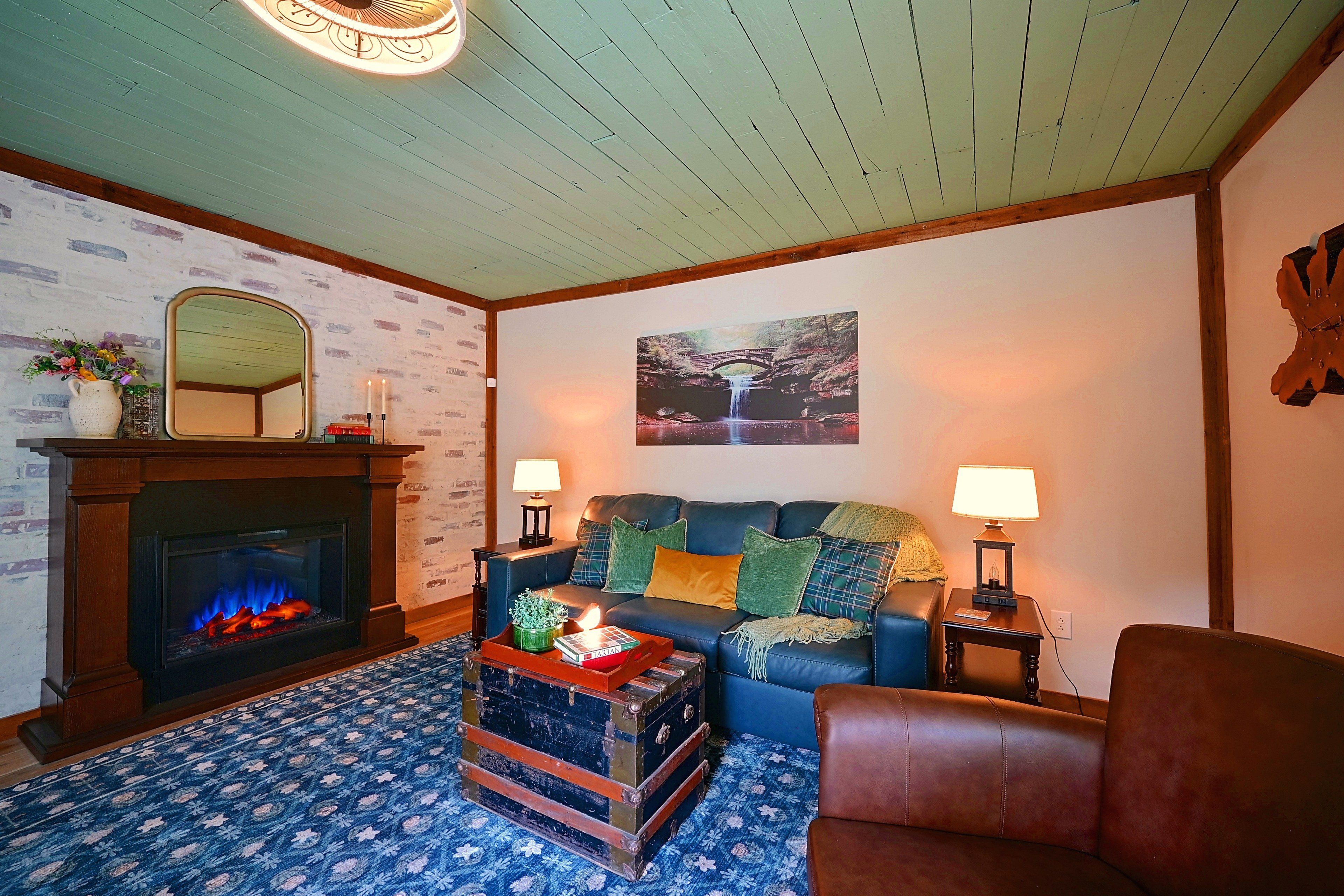 A cozy living room with a fireplace, a blue sofa, a patterned rug, and a wooden coffee table.