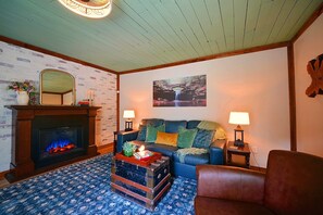 Ein gemütliches Wohnzimmer mit Kamin, einem blauen Sofa, einem gemusterten Teppich und einem Holztisch.