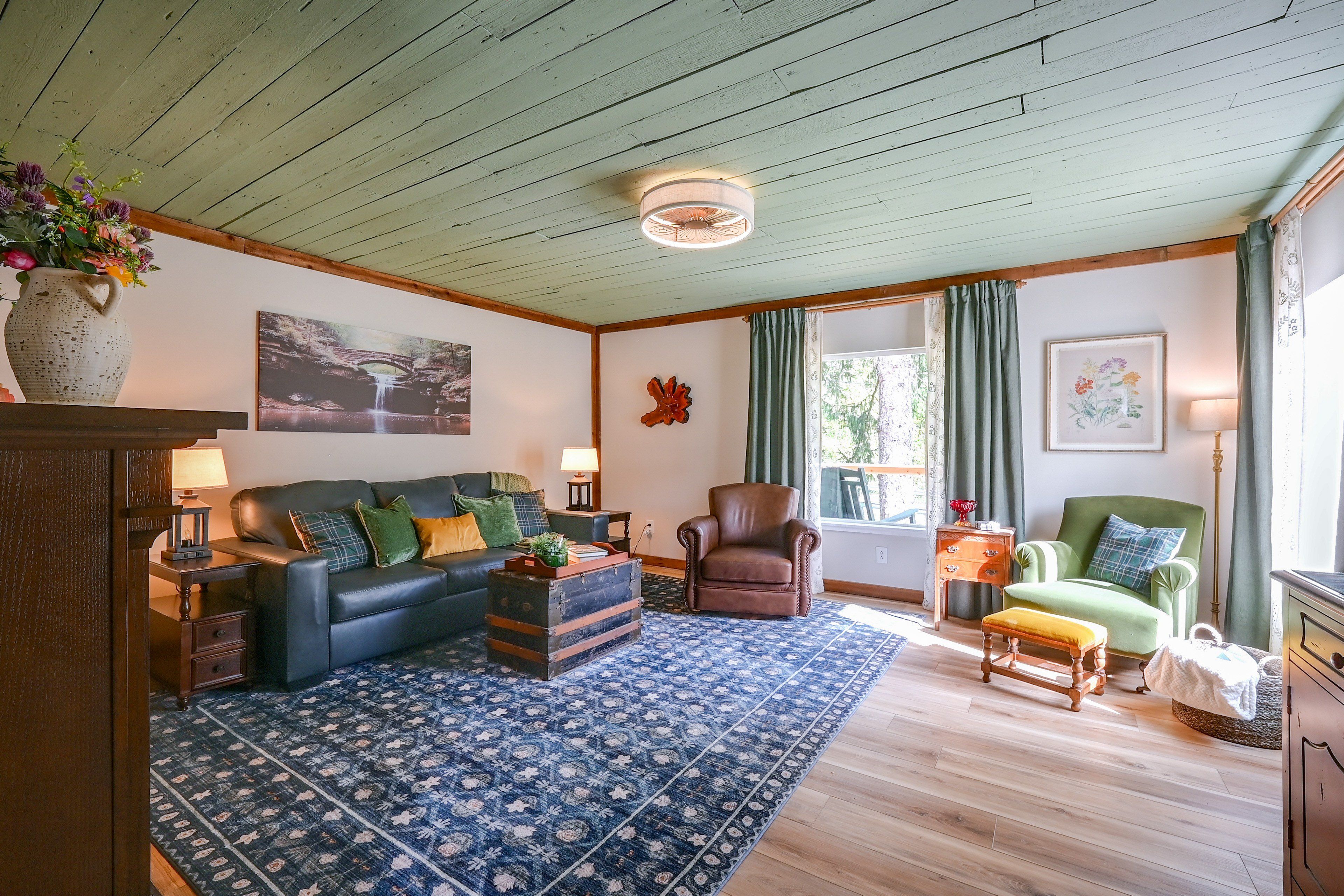 A living room with a blue patterned rug, a leather sofa, a wooden armchair, and a green armchair.