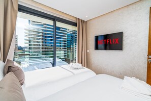 A hotel room with a large bed, a view of a high-rise building, and a sign for Netflix. - New luxury apartment near the TGV station (Tanger)